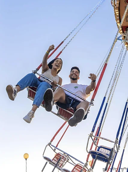 Casal sorrindo em um brinquedo de balanço da Nicolândia, com o céu azul ao fundo